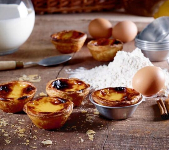 Pasteis de Nata and the raw ingredients strewn on a wooden table