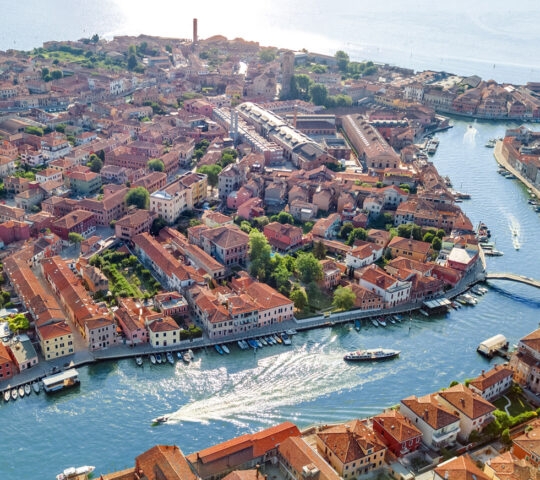 High-angle aerial view of a canal in Venice with red-roofed houses and boats moving through the water.