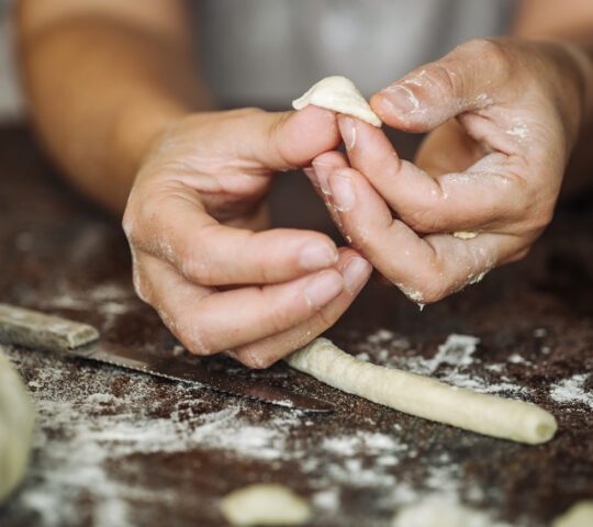 Hands crafting fresh orecchiette pasta from dough on a floured table during luxury Puglia tours.