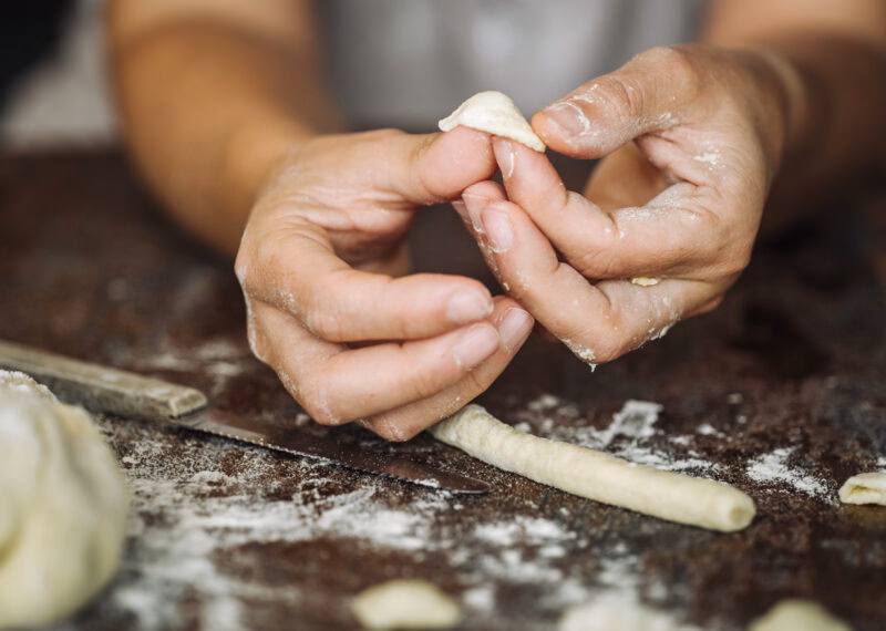 Hands crafting fresh orecchiette pasta from dough on a floured table during luxury Puglia tours.