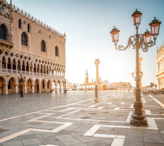 View of the Doge's Palace and an ornate black street lamp in a sunlit square in Venice, Italy.