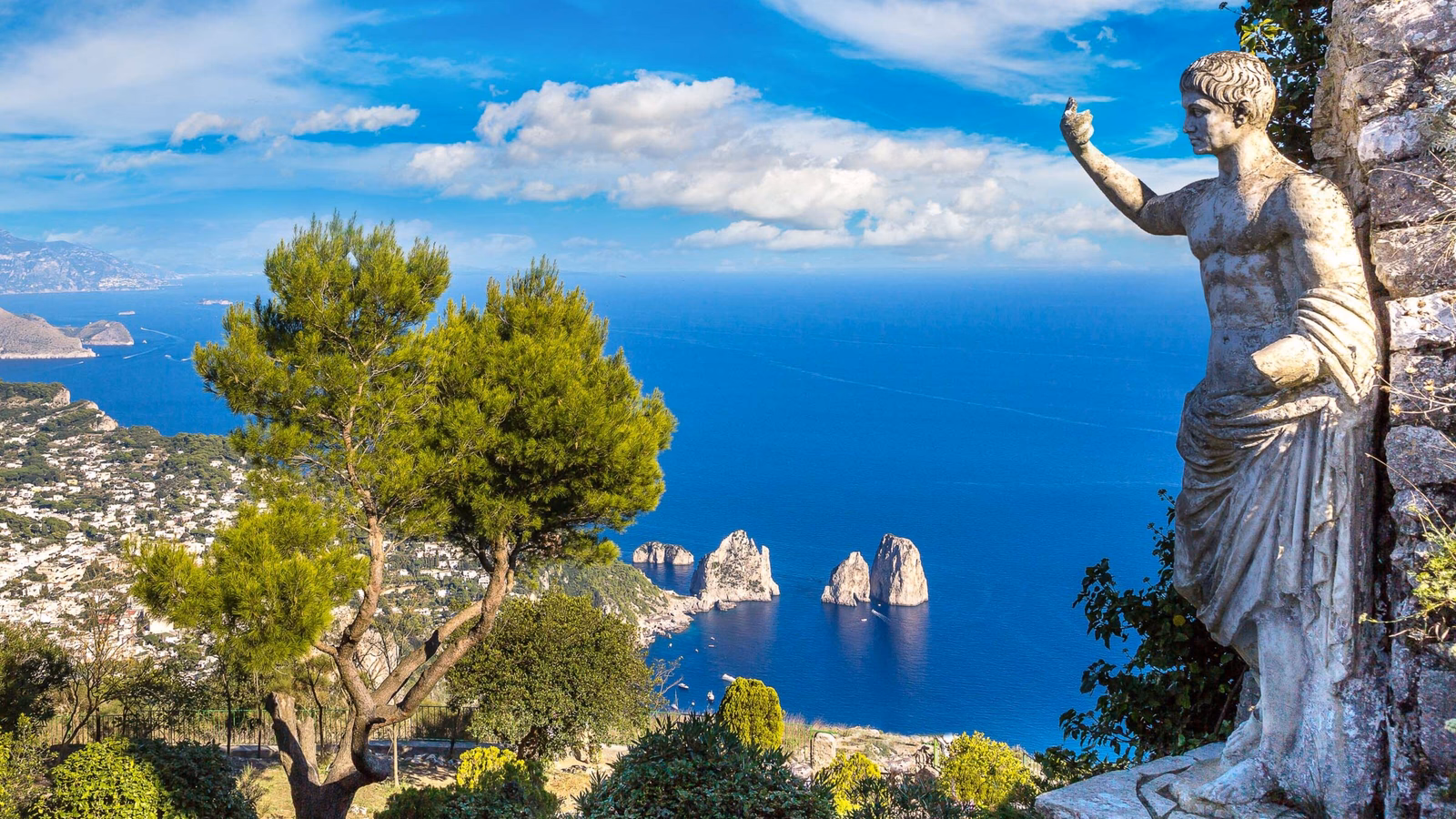 Stone statue of a Roman emperor overlooking a high coastal view of the sea and iconic rock stacks in Capri.