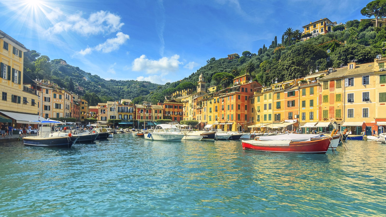 Sunny view of a Mediterranean harbor with docked boats and vibrant buildings under a blue sky.