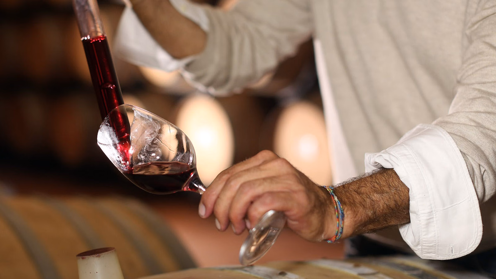Close-up of red wine being poured from a glass tube into a wine glass in a cellar.