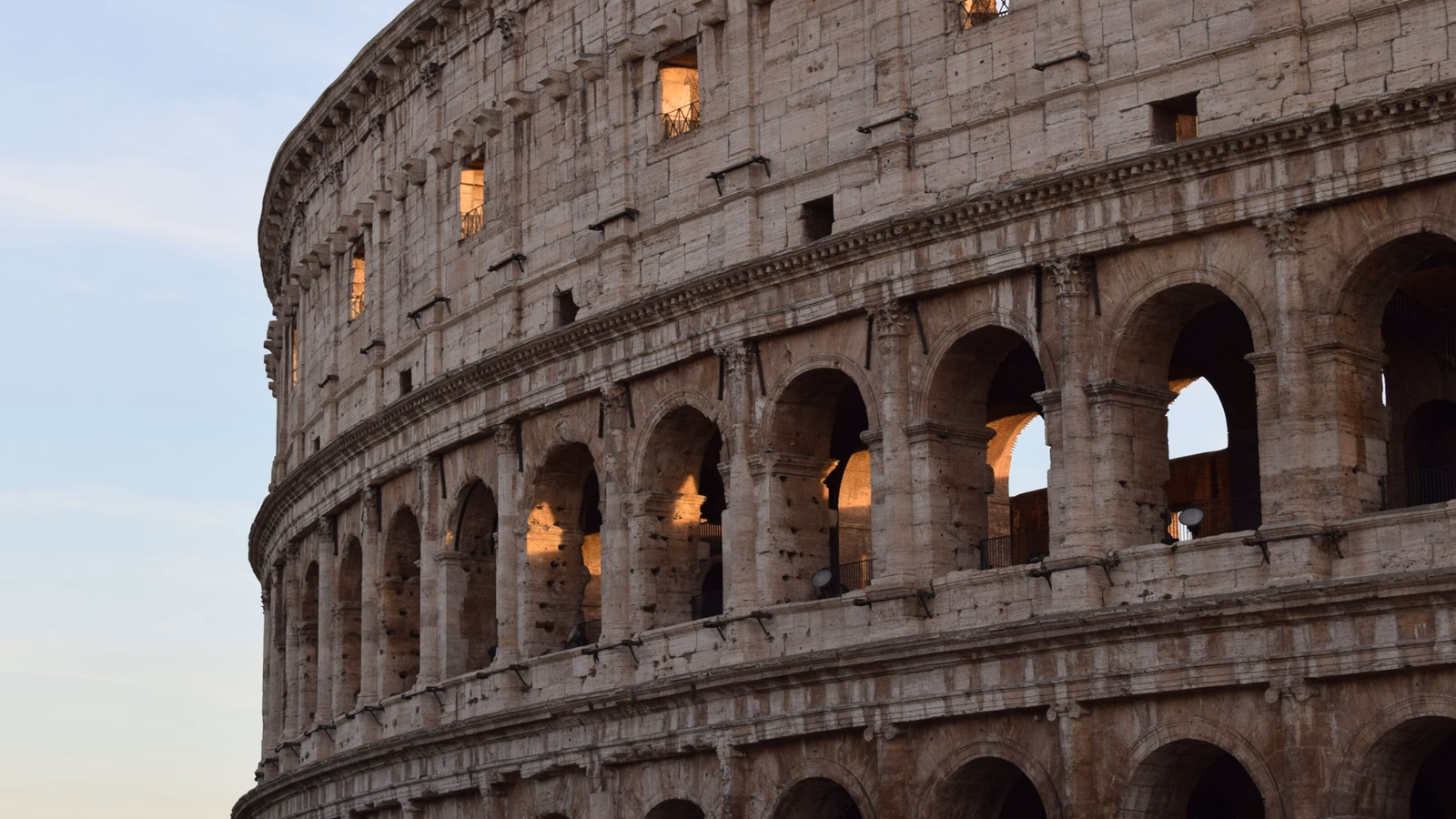 Detail of the Colosseum arches with warm light glowing from within at dusk.