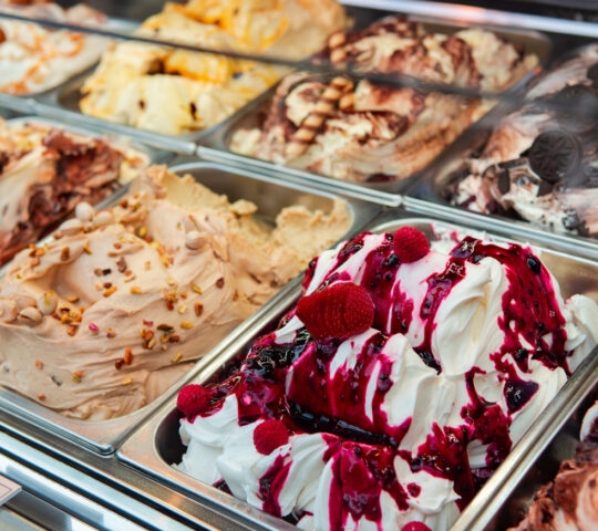 A close-up view of various flavors of Italian gelato in a display freezer.