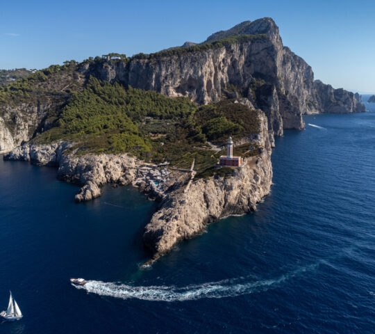 aerial view of a sailboat, a motorboat and a lighthouse on the coast of Capri