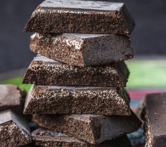 A vertical stack of thick, dark chocolate squares with a rough, crystalline texture.