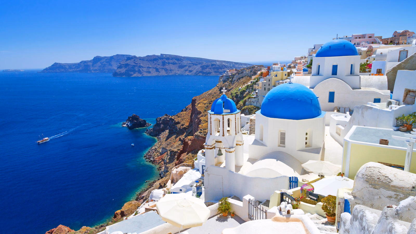 White buildings with bright blue domes on a cliffside overlooking the Aegean Sea in Santorini, Greece.