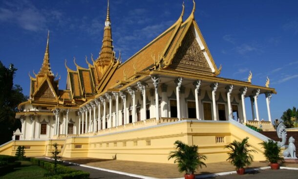A grand palace building with golden tiered roofs and white columns under a clear blue sky.