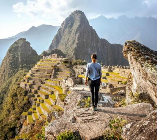 Traveller standing on a rock overlooking Machu Picchu, Peru