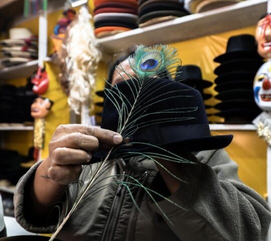 Market trader holding up a peacock tail feather and black brimmed hat
