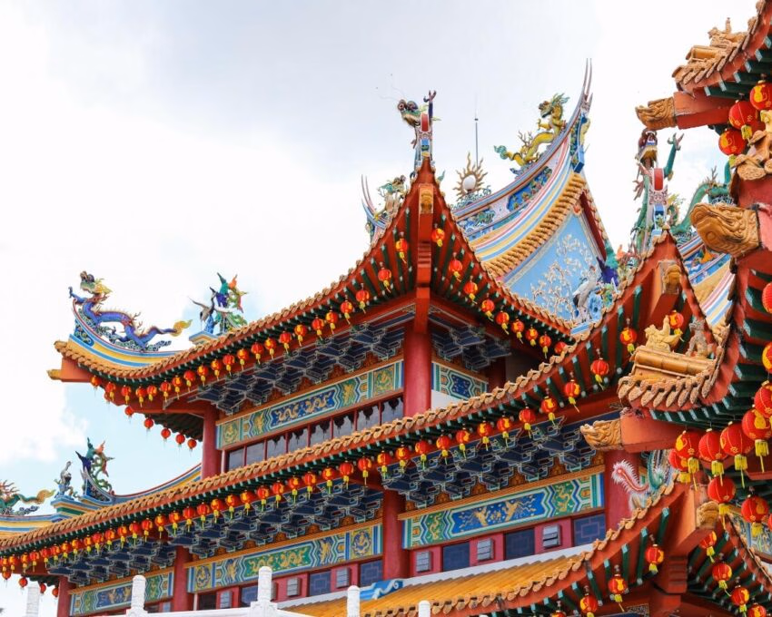 Close-up of a multi-tiered Chinese temple roof decorated with colorful dragon figures and hanging red lanterns.