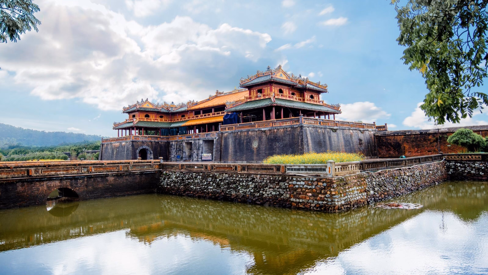 A large historic stone gatehouse and palace complex reflected in the still water of a surrounding moat.