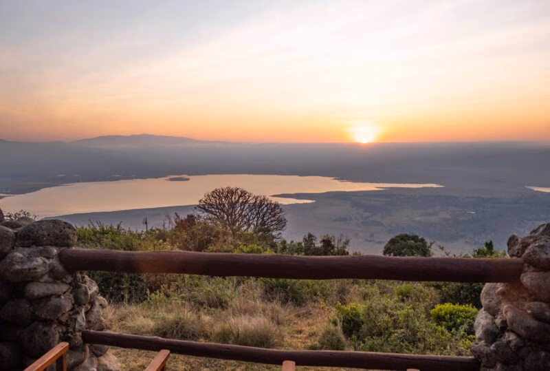 A luxury Ngorongoro Crater safari sunset viewed from a stone lodge balcony overlooking the lake and distant mountains.
