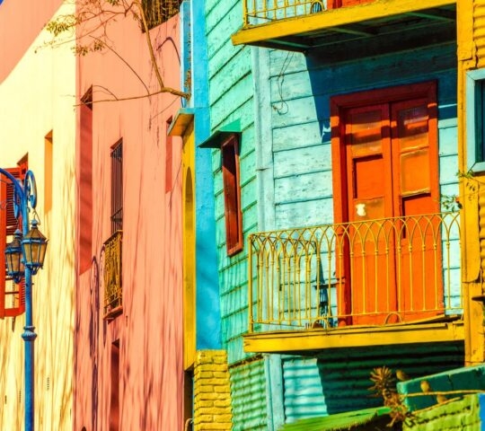 Vibrant multi-colored buildings with metal balconies and a decorative blue street lamp in bright sunlight.