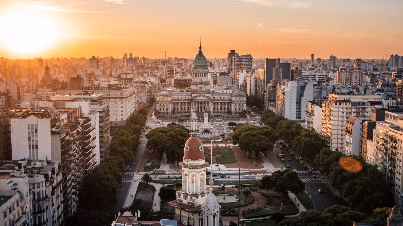 High-angle view of a large city plaza leading to a domed government building under a bright sunset sky.