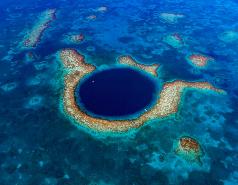 Aerial view of a large circular deep blue marine sinkhole surrounded by a shallow turquoise coral reef.