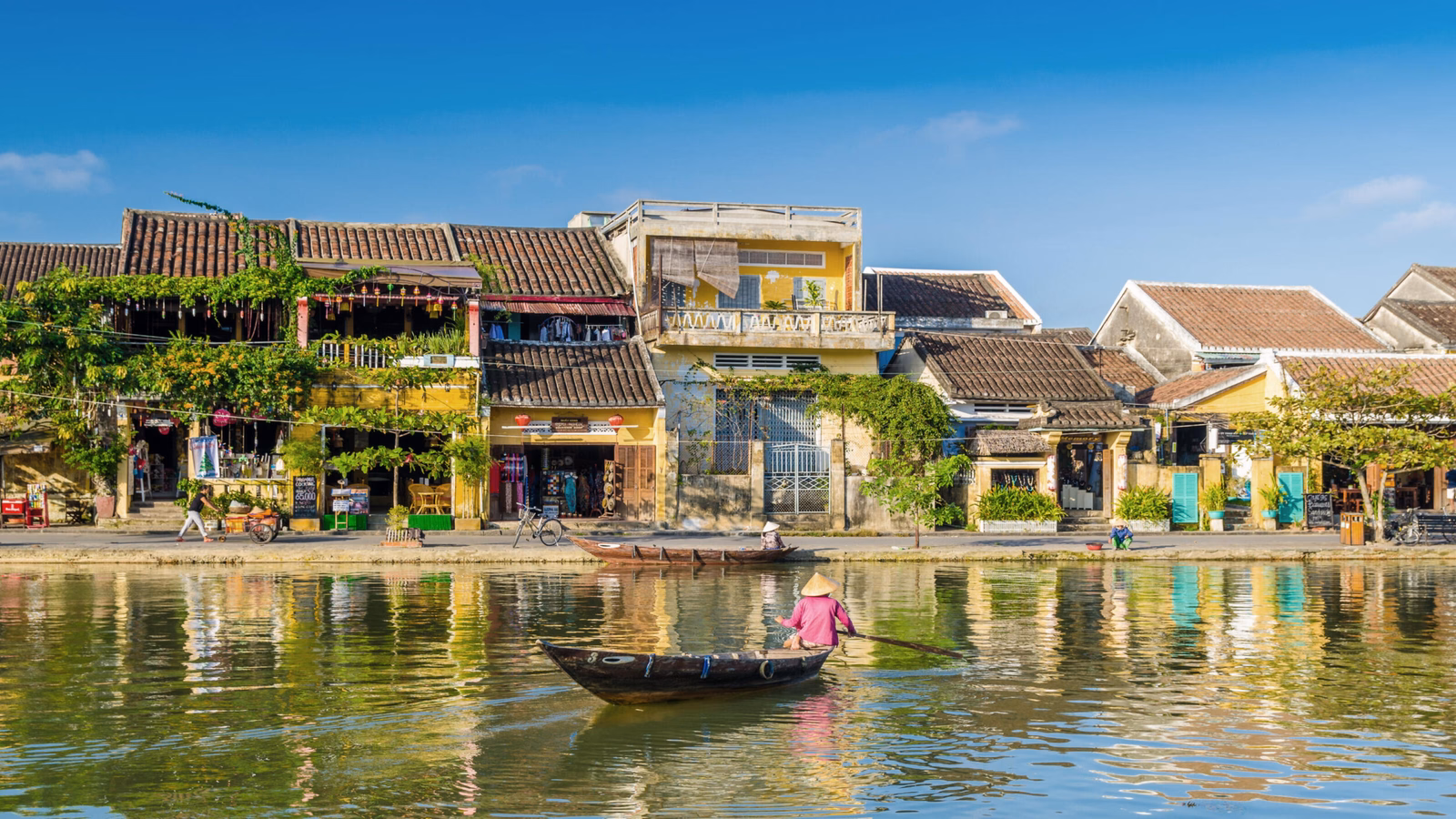 A person in a boat on a river reflecting the yellow historic buildings of an ancient waterfront town.