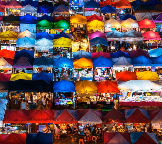 High-angle view of many colorful glowing tents at a crowded night market.