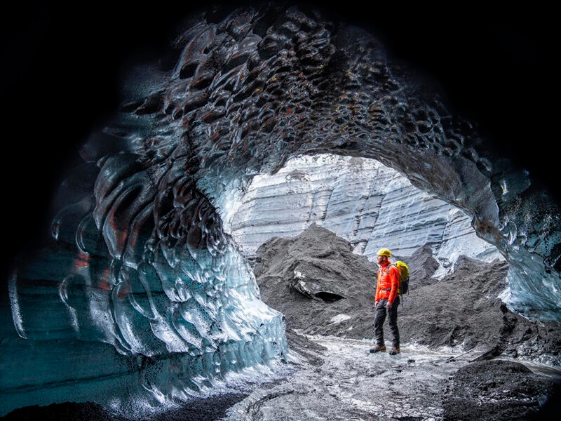 Hiker standing by ice cave at glacier in Iceland