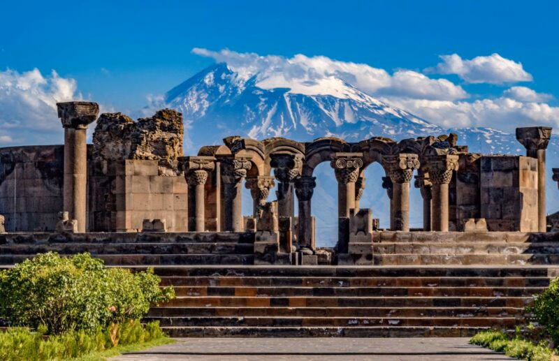 Ancient stone arches and columns with a mountain backdrop on luxury Central Asia trips.