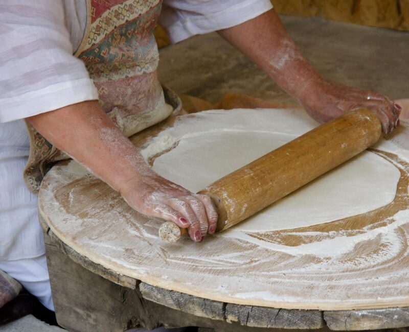 Hands rolling out thin dough on a wooden table during luxury Central Asia holidays.
