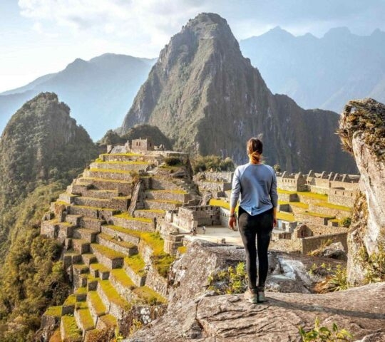 A person looking out over the historic ruins of Machu Picchu surrounded by steep green mountains.