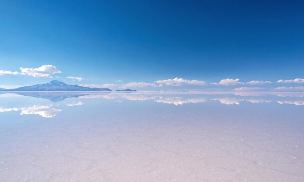 A mirror-like reflection of a blue sky and white clouds on the surface of the Salar de Uyuni salt flats.