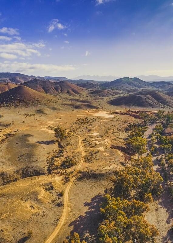 Aerial view of a dirt road winding through dry, rolling hills and sparse vegetation.