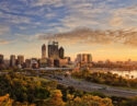 Gold warm sun light hitting CBD of Perth city as seen from Kings park with green trees and highway entering the city.