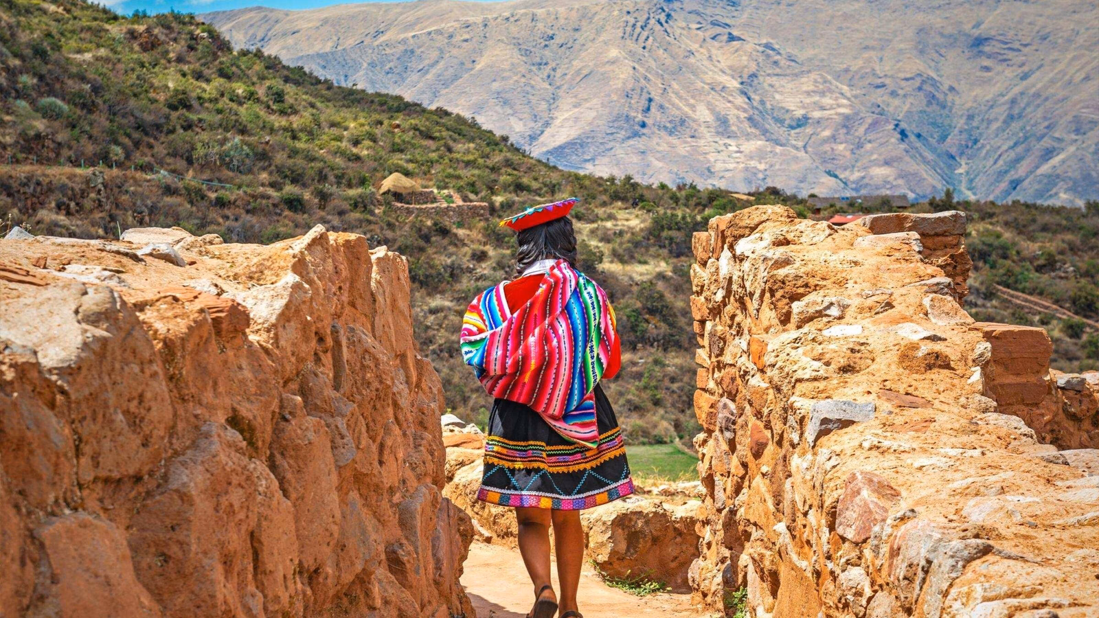 Quechua Indigenous Woman in traditional clothes walking along ancient Inca Wall