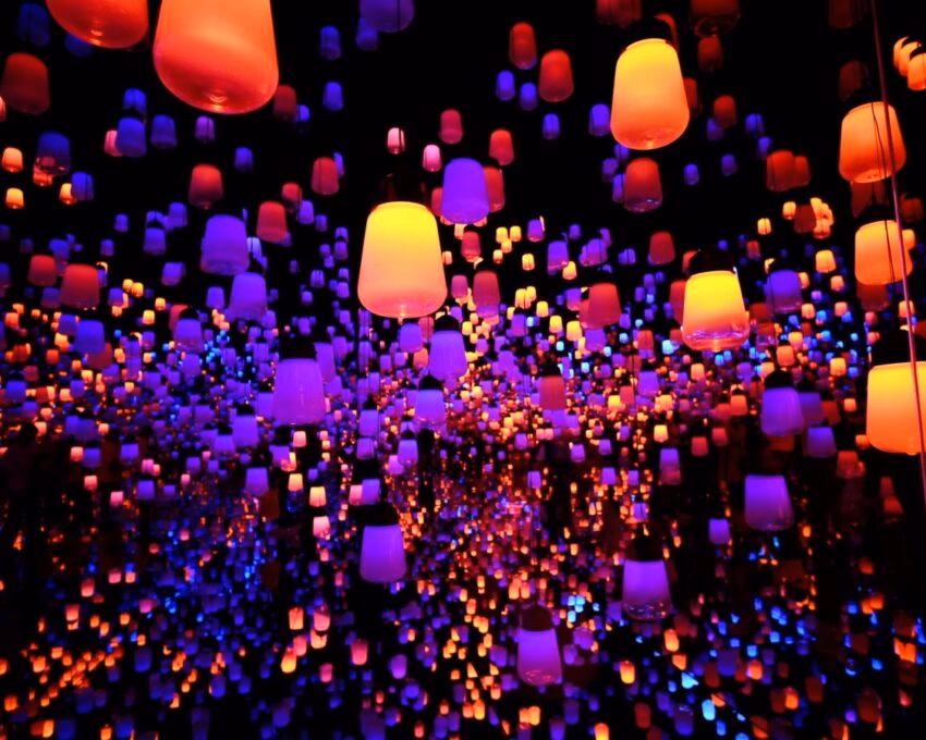 Hundreds of illuminated orange, red, and blue lanterns hanging in a dark space, creating an immersive, infinite reflection effect.