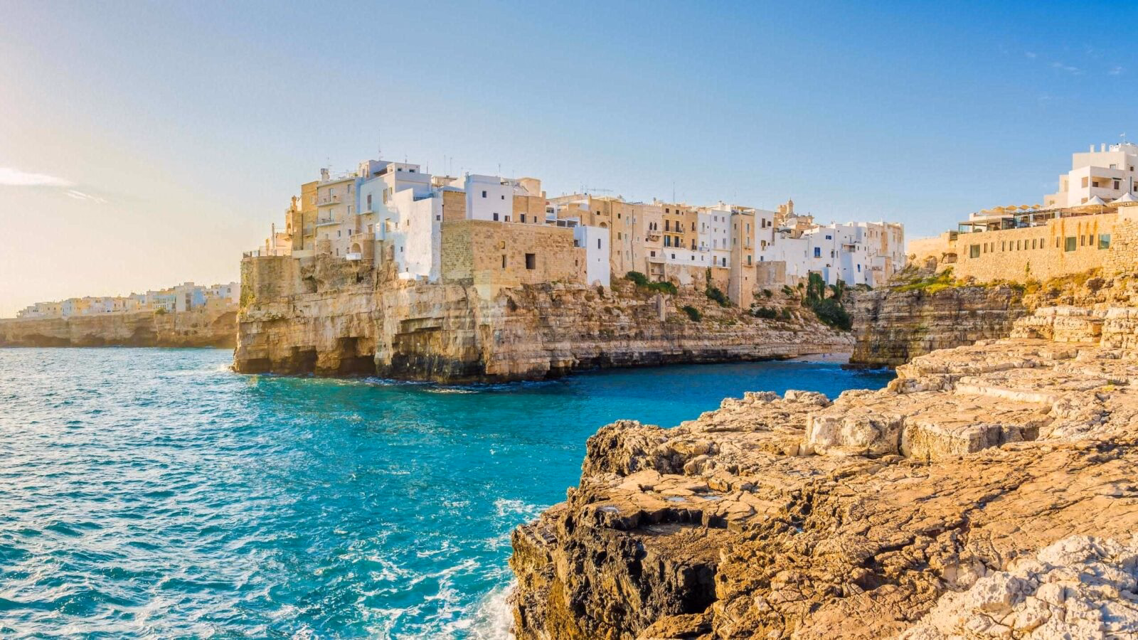 Coastal town buildings on high limestone cliffs above turquoise water during luxury Puglia holidays.