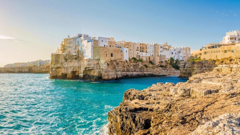 Coastal town buildings on high limestone cliffs above turquoise water during luxury Puglia holidays.