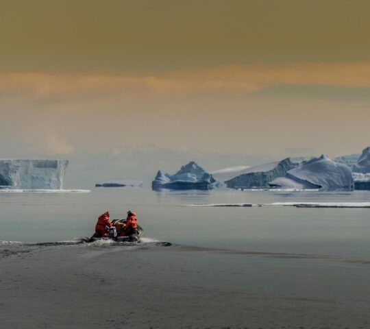 Two people on a Zodiac in Antarctica cruising iceberg-strewn waters.