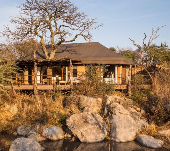 External shot of suite at Mwiba Lodge, a building with outdoor seating area in front of a river