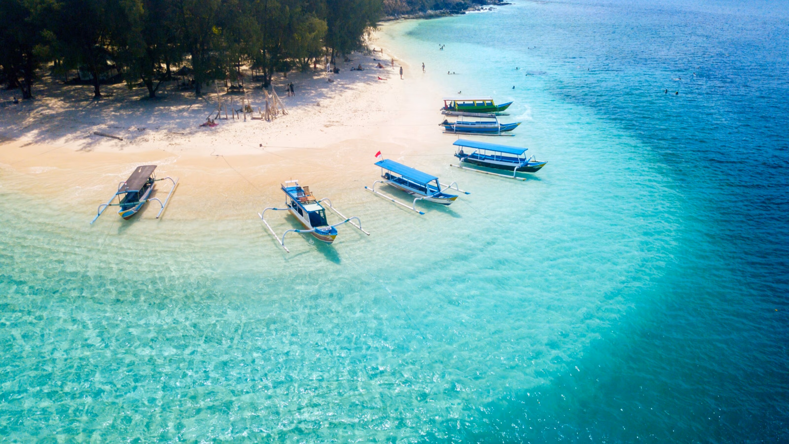 Aerial view of turquoise ocean water and a white sand beach with several small boats anchored near the shore.