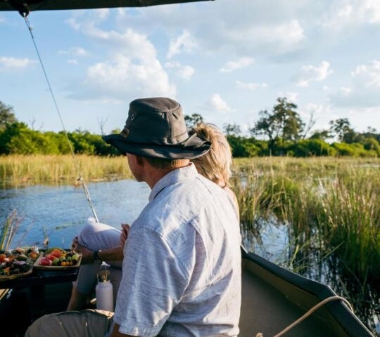 A couple sit on a boat going down the river in Linyanti