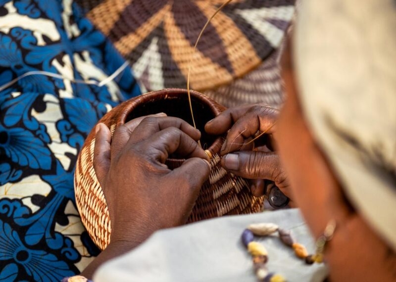 A woman weaves a basket by hand using traditional methods