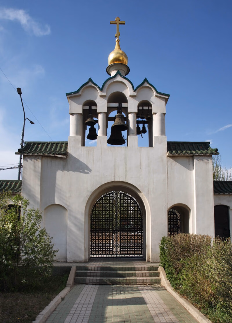 A white arched bell tower with a golden dome, a historical site seen on luxury Mongolia tours.