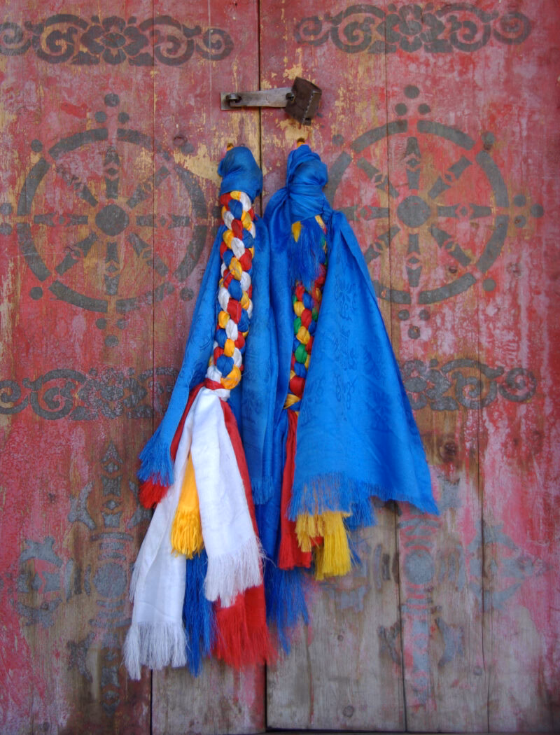 Braided silk scarves draped over a red wooden door, reflecting the traditions of luxury Mongolia holidays.