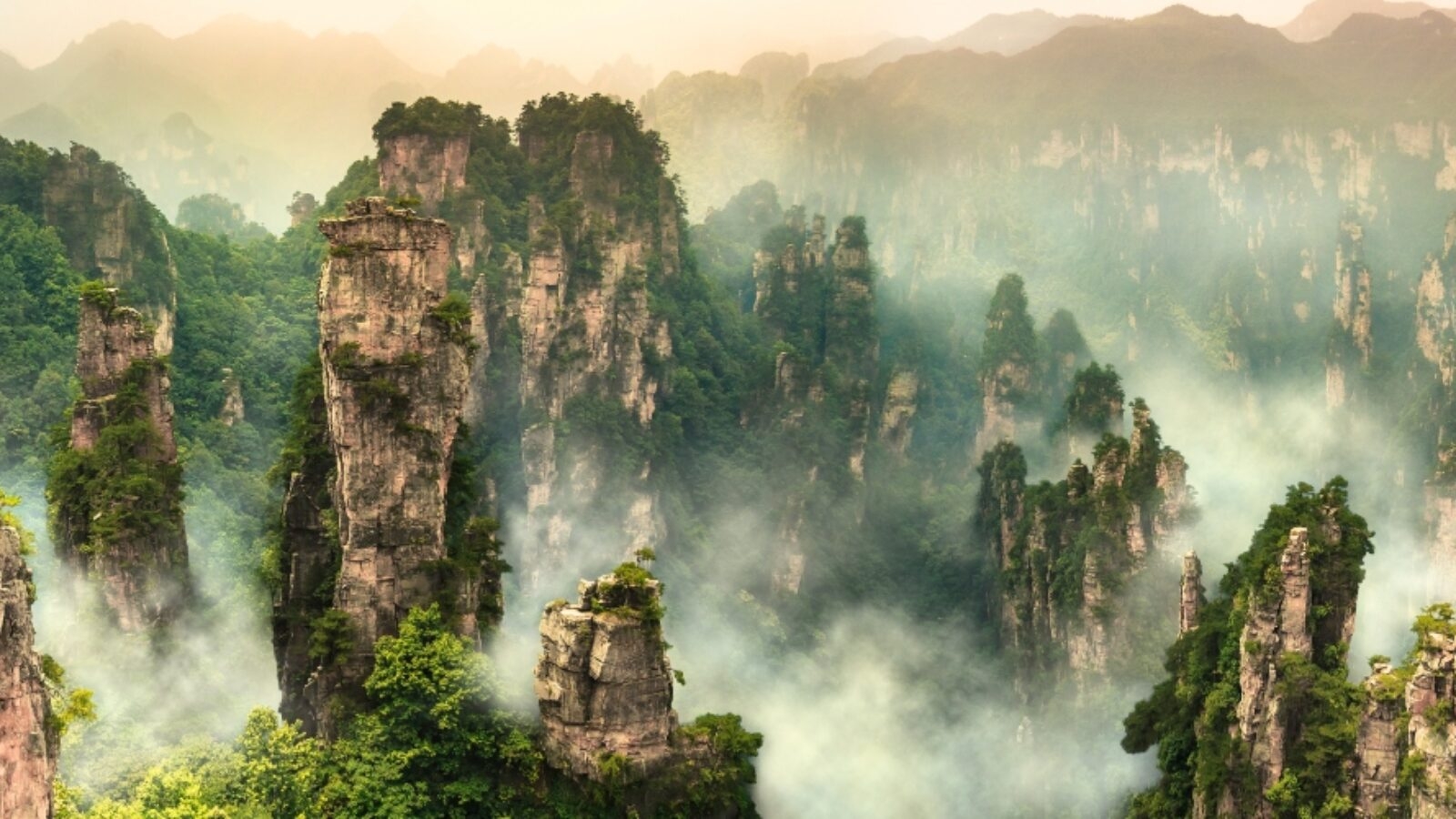 Tall sandstone pillars surrounded by mist and green trees during luxury Asia grand tours.
