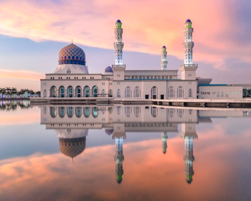 A grand white mosque with minarets reflected in still water at sunset during luxury Asia grand tours.