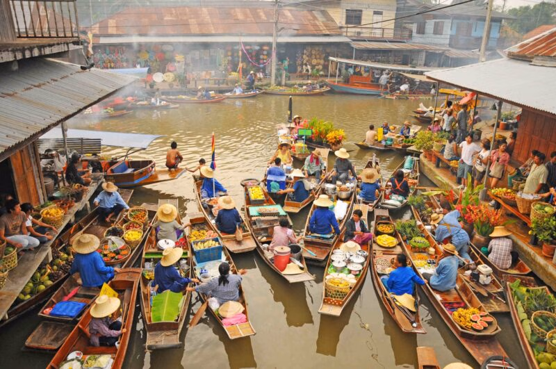 Overhead view of many small wooden boats carrying produce and vendors navigating a narrow waterway at a floating market.