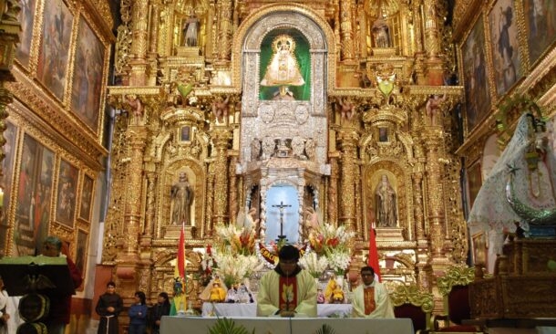 An elaborate golden altar with religious statues and paintings serves as the backdrop for a ceremony with priests.