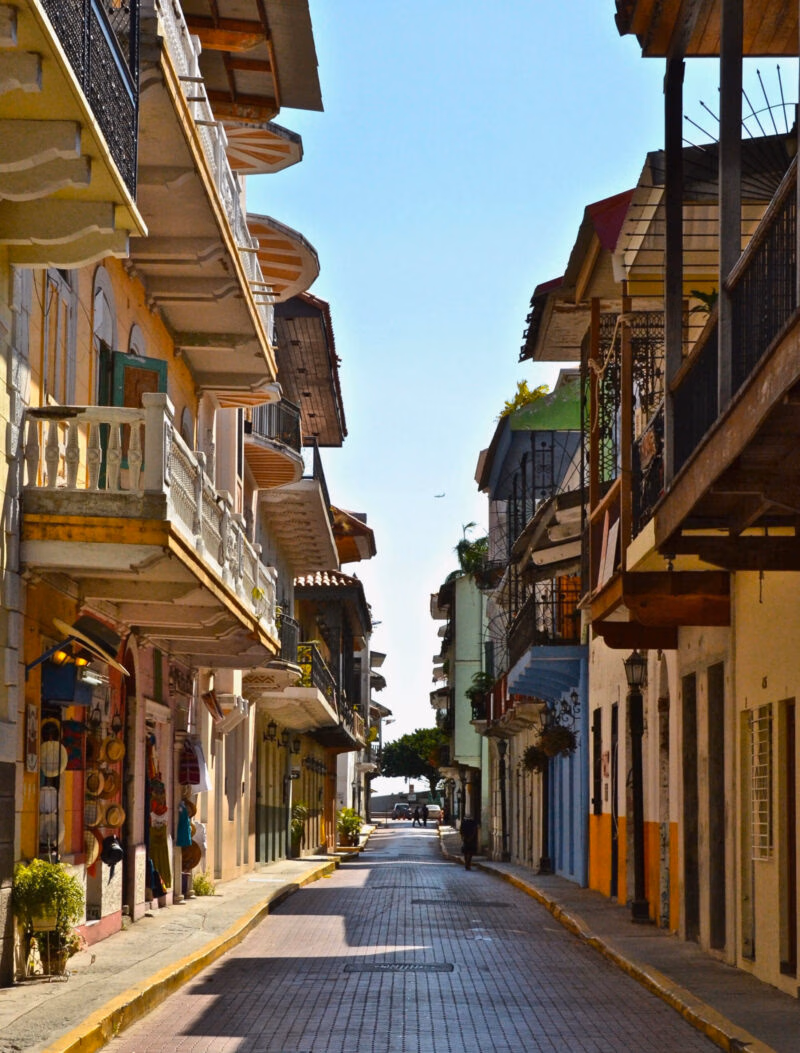 A narrow street in Panama City lined with multi-story colonial buildings featuring colorful facades and balconies.