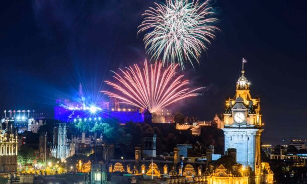Colorful fireworks display over Edinburgh Castle and the city's historic landmarks at night.