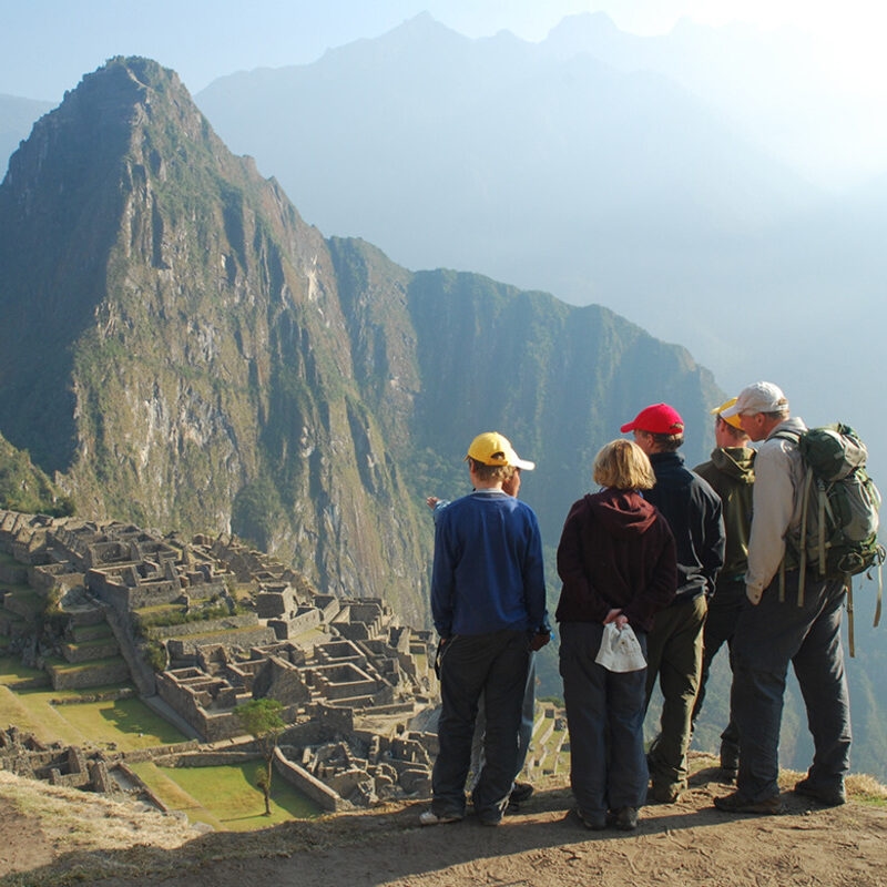 A group of five hikers looking out over the ancient stone city ruins of Machu Picchu in the mountains.