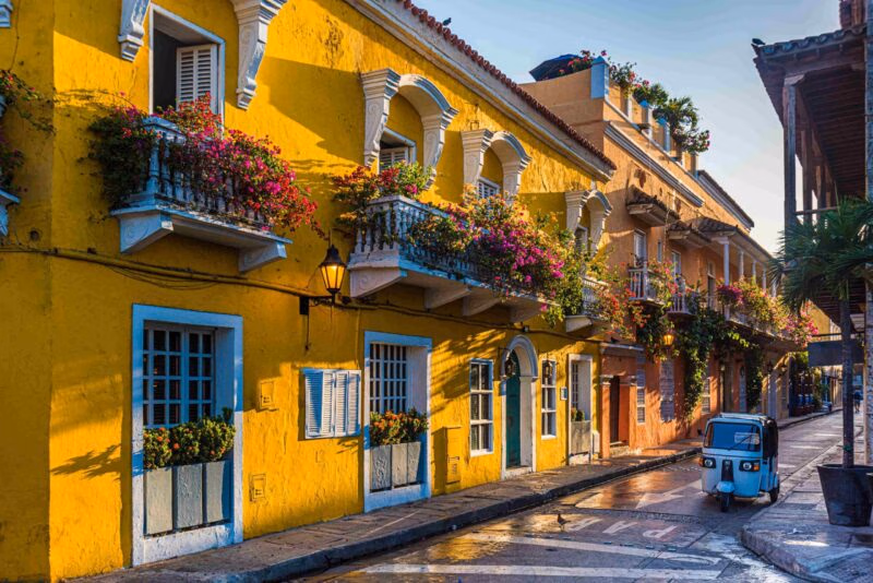 A beautiful street with bright yellow Colonial-style buildings and a motorised tuk tuk on the road in Cartagena, Colombia